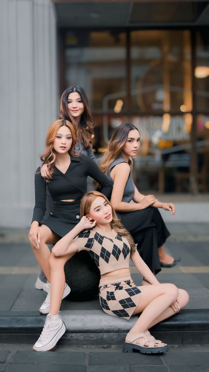 Four fashionable young women pose confidently outdoors in an urban environment.