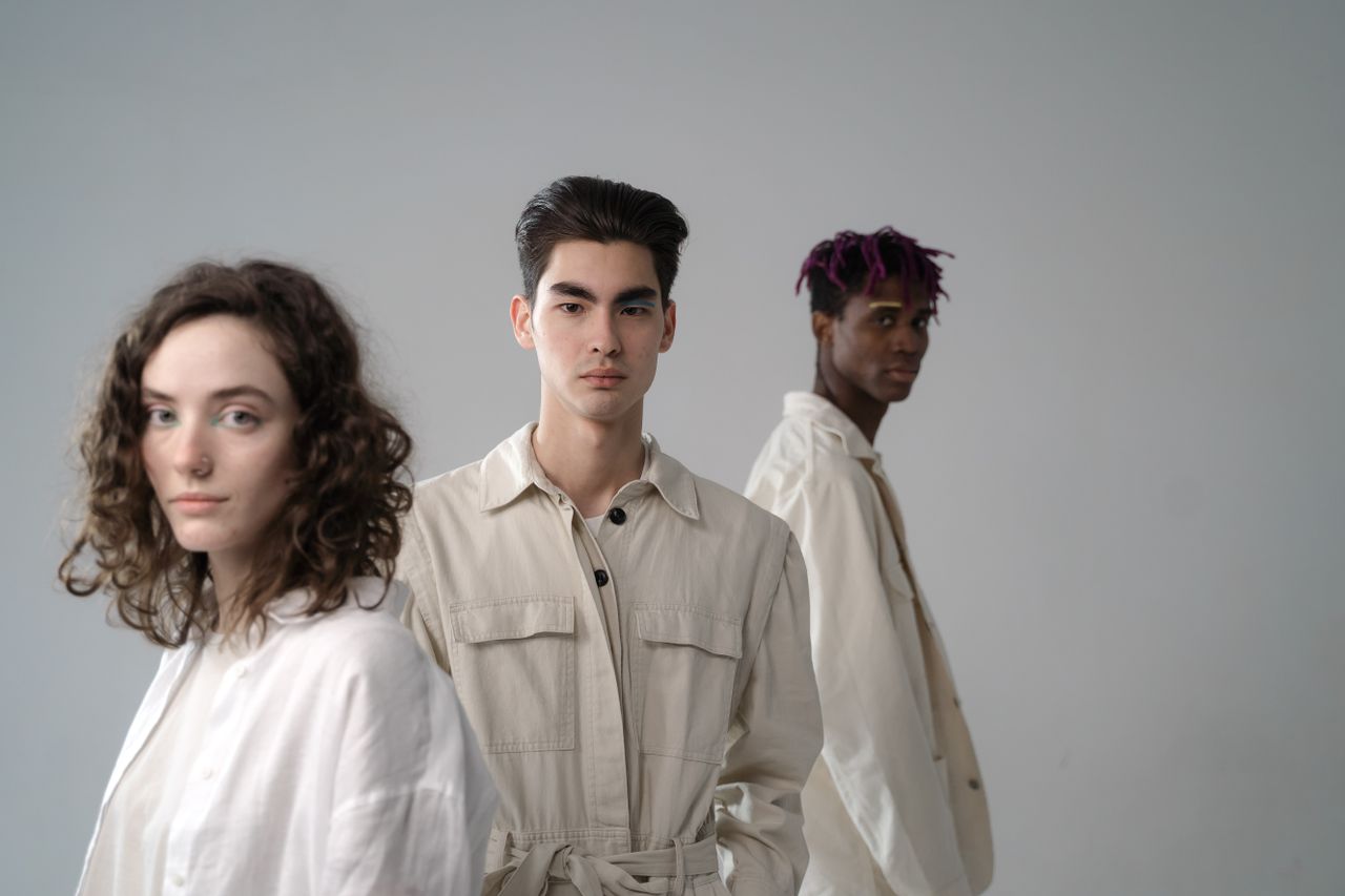 Group of diverse multiethnic young people wearing light beige and white cotton clothes standing in studio and looking at camera on gray background